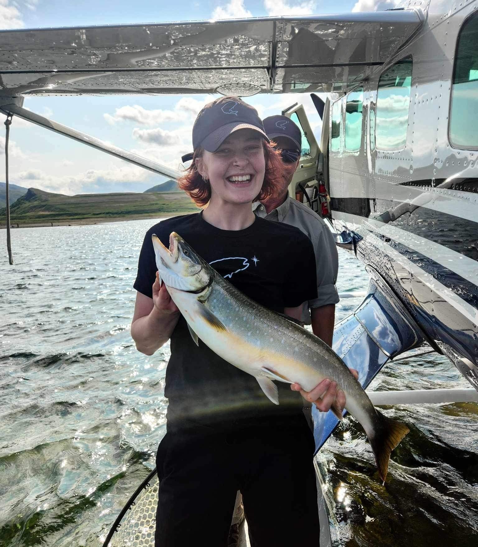 Juliana Dyke holding an Arctic Charr beside a floatplane